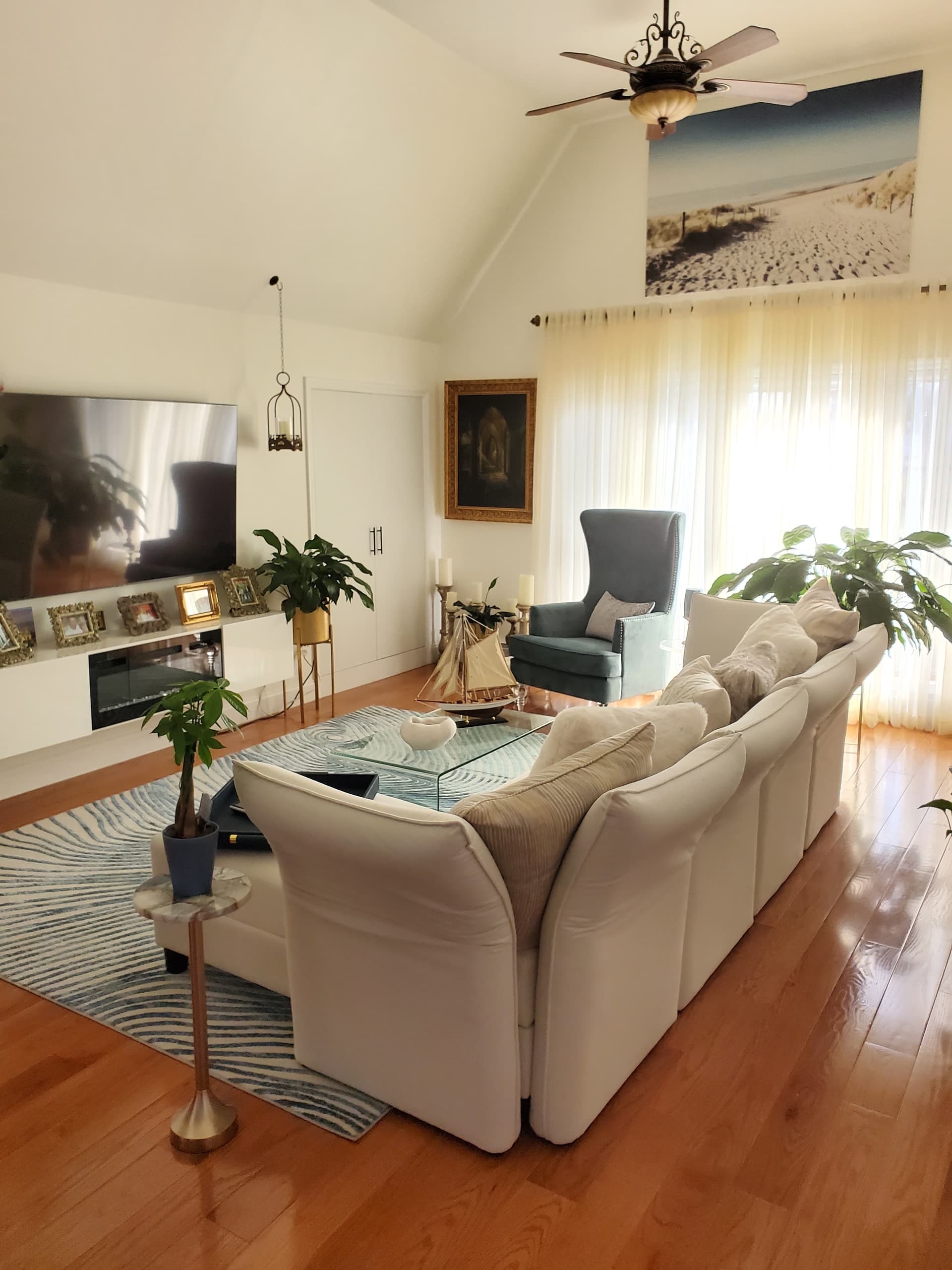 Coastal vaulted living room with white sectional seating, blue accent chair, sheer curtains, and coastal artwork — designed by Renata Glaz