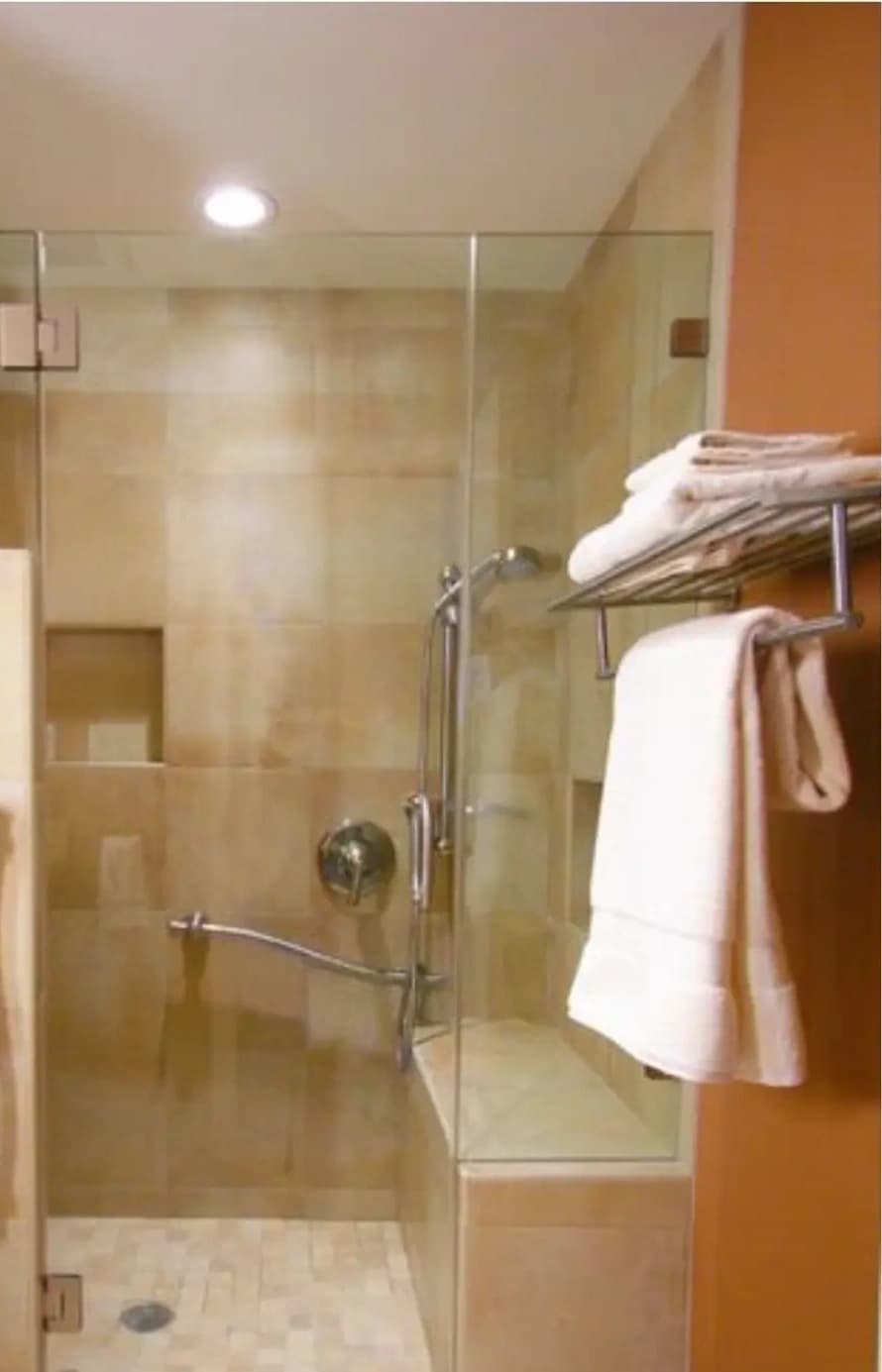 Walk-in shower with built-in bench, stone tile, and supportive grab bars designed for safer daily routines — by Renata Glaz